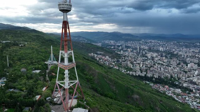 Aerial view of the Funicular Restaurant at Mtatsminda Park during sunset. Dynamic drone shot of a TV tower with Tbilisi city in the background.