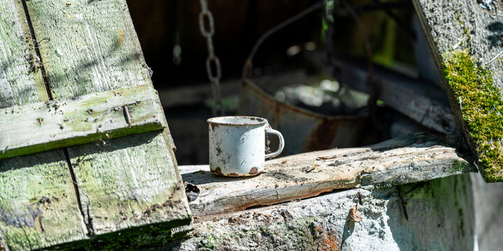 Rusty enamel mug sitting on an old wooden plank of a wellhead, highlighting rural vintage style, tradition, and forgotten items