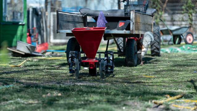 Red seeder attached to a tractor trailer, ready for spring planting in a backyard garden, symbolizing cultivation and new beginnings
