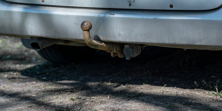 Rear view of a gray car featuring a heavily rusted trailer hitch ball and electrical connection, with an exhaust pipe visible