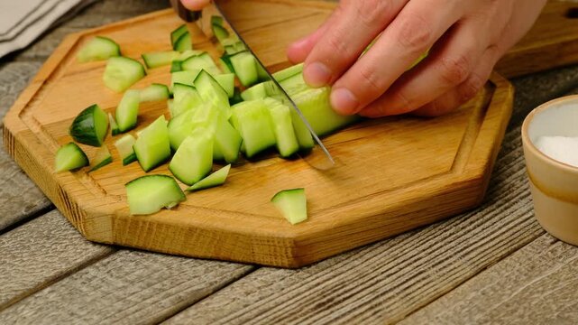A woman slices a long cucumber on a wooden board with a knife. Step-by-step recipes, video recipes