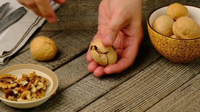 Cracking a walnut with tongs on a gray wooden background. Ingredients for cooking. Video recipes. 
