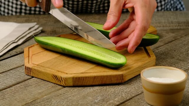 A woman cuts a long cucumber into halves with a knife on a wooden board. Step-by-step recipes, video recipes