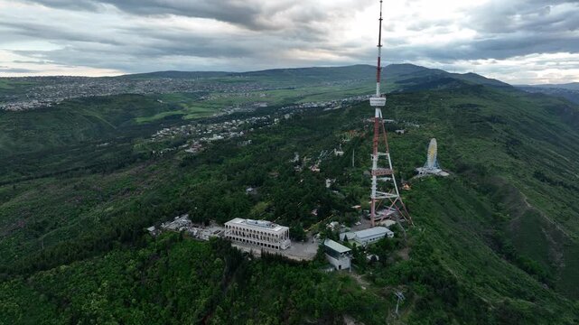 Aerial view of the Funicular Restaurant at Mtatsminda Park during sunset. Dynamic drone shot of a TV tower with Tbilisi city in the background.