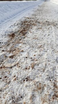 Snow cleared pedestrian path alongside highway, showing salted and grit strewn surface, high plow berm, tire tracks and compacted