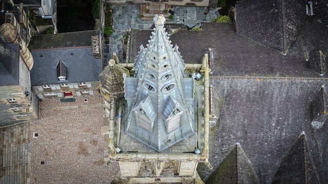 Aerial view of the Gothic spire of Eglise Saint-Melaine de Morlaix surrounded by historic stone rooftops and a cobblestone courtyard in Morlaix, Bretagne, France.