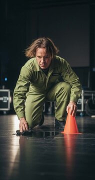 Man kneeling with orange cone on stage with dark background