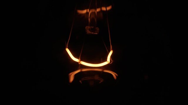 Detailed tungsten filament of an incandescent light bulb glows intensely with a warm orange light in the dark. Concept of innovation, creative thinking, bright ideas, energy, and old technology.