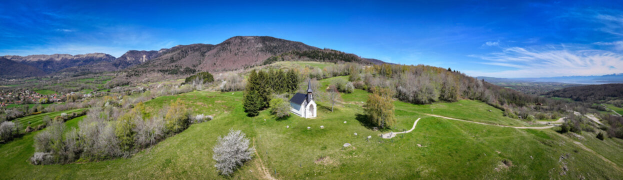 Aerial view of the Chapelle Notre-Dame de Riantmont on a green hill with mountains in the background in Vesancy, Auvergne-Rhone-Alpes, France.