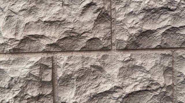 Close-up textured stone facade panels, dark brown natural stone with chiseled rough surface, modular block layout with visible