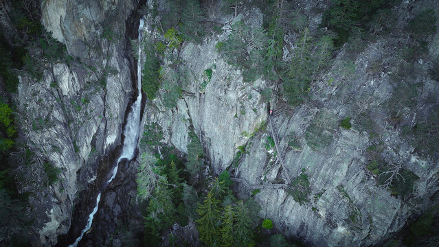 Aerial view of Gorges du Dailley waterfall cascading down a steep rocky cliff with wooden stairs and pine trees in Salvan, Valais, Switzerland.