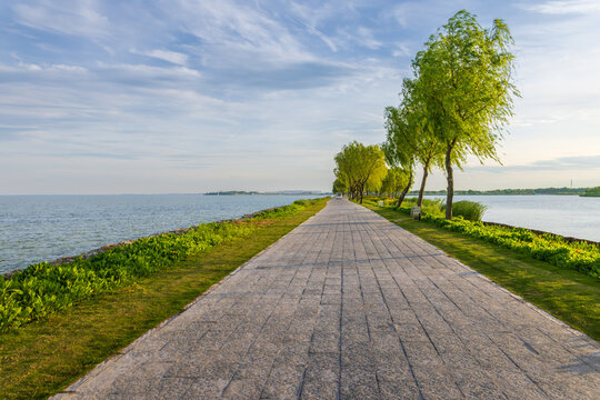 Yongfang Dyke at Chaohu Lake in Hefei: Blue Water and Sky Reflect the Long Dyke, Green Trees Accompany Tourists
