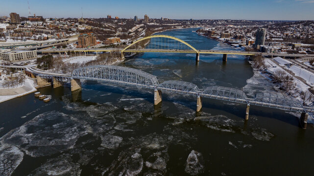 Aerial view of the Daniel Carter Beard Bridge and Taylor-Southgate Bridge over the frozen Ohio River with floating ice and snowy banks in Cincinnati, Ohio, United States.