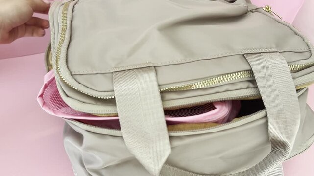 Woman's hands using travel organizer cubes for packing a suitcase, zipping up the weekender bag on a pink background, showcasing efficient vacation preparation
