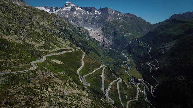 Aerial view of the winding switchbacks of the Grimsel Pass surrounded by steep alpine slopes and distant glaciers in Obergoms, Valais, Switzerland.