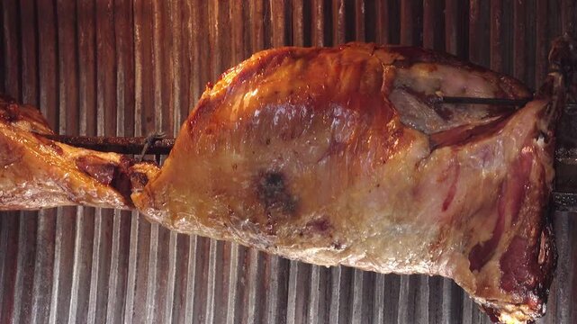 In the oven, the whole animal carcass is roasted and slowly rotated on metal spits, revealing crisp, browned skin, fat, and meat, a traditional barbecue method.