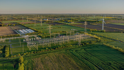 Electrical substation with large-scale battery energy storage system (BESS) installation, power lines, and wind turbines in the background. © snapshotfreddy