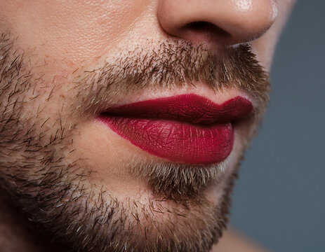 Close-up portrait of a man with a beard wearing red lipstick on his lips to express his unique gender identity.