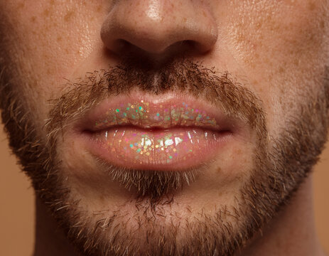 Close-up portrait of a man with a beard and freckles wearing glitter gloss on his lips for unique gender identity expression.