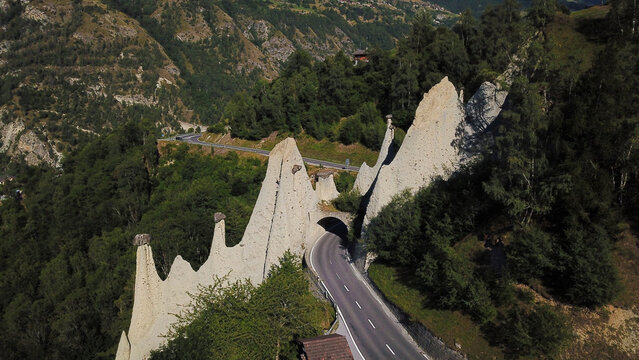 Aerial view of the Pyramides d'Euseigne rock formations and a winding mountain road passing through the alpine forest in Heremence, Valais, Switzerland.