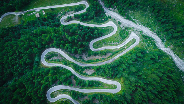 Aerial view of a winding serpentine mountain road snaking through a dense green pine forest in the Swiss Alps, Heremence, Valais, Switzerland.