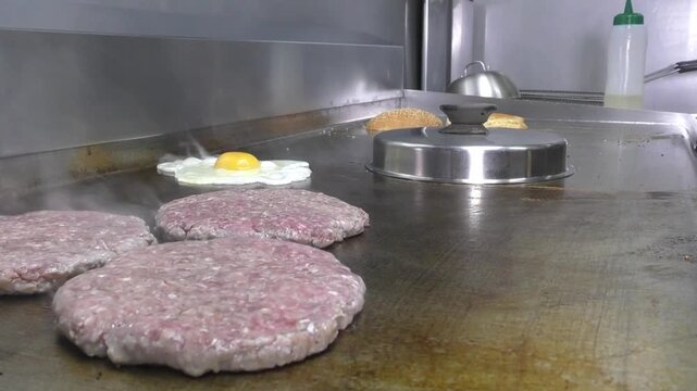 Preparazione di un panino hamburger su piastra. Panino hamburger grigliato con pancetta, cipolla glassata, formaggio e uova