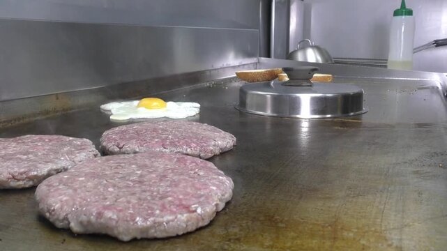 Preparazione di un panino hamburger su piastra. Panino hamburger grigliato con pancetta, cipolla glassata, formaggio e uova