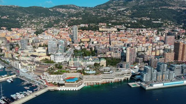 4K aerial view of Monaco vertical cityscape with Casino Square, Port Hercule, rainbow rooftop heliport, dense high-rise towers climbing the mountainside above the Mediterranean coast.