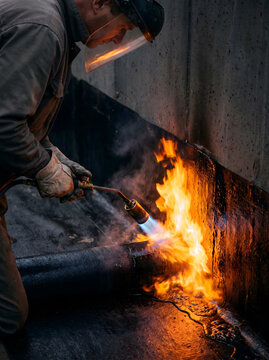 Worker applying torch-on bitumen waterproofing membrane at concrete wall