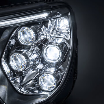 Close-up of modern LED headlight with multiple projector lenses on dark background