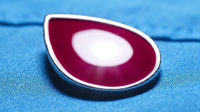 Glossy red teardrop shape with moving light reflection, close up on blue fabric, for abstract design.