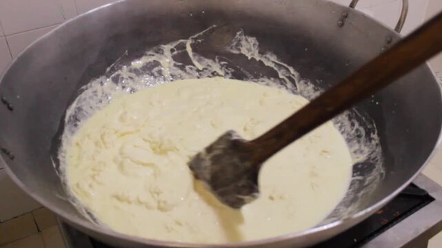 An unrecognizable person is adding whey to a cheese mixture and then stirring it to produce typical Quesillos inside a restaurant in Yaguara, Huila, Colombia. Concept of handmade and Colombian food