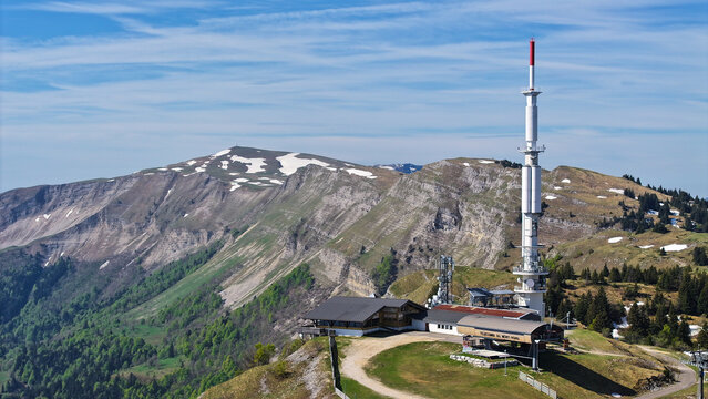 Aerial view of Col de la Faucille featuring the telecommunications tower and snowy mountain ridges under a clear blue sky in Gex, Auvergne-Rhone-Alpes, France.