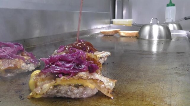 Preparazione di un panino hamburger su piastra. Panino hamburger grigliato con pancetta, cipolla glassata, formaggio e uova