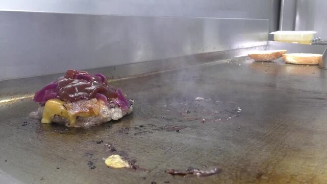 Preparazione di un panino hamburger su piastra. Panino hamburger grigliato con pancetta, cipolla glassata, formaggio e uova