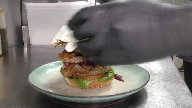Preparazione di un panino hamburger su piastra. Panino hamburger grigliato con pancetta, cipolla glassata, formaggio e uova