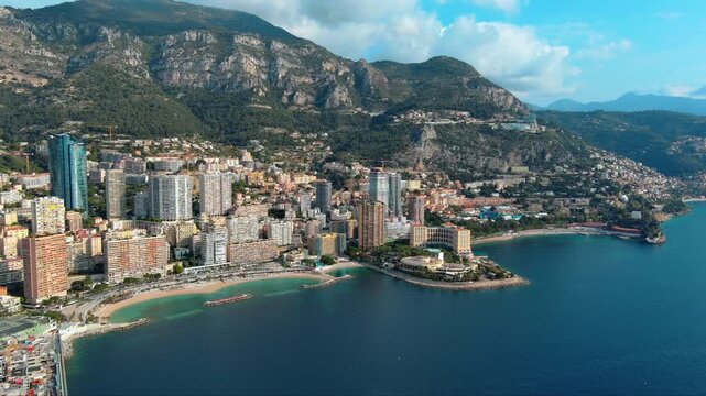4K aerial view of Larvotto beach and Monte-Carlo Bay in Monaco with Tour Od&eacute;on skyscraper, luxury residential towers, Mediterranean Sea and Maritime Alps backdrop. French Riviera coastline.
