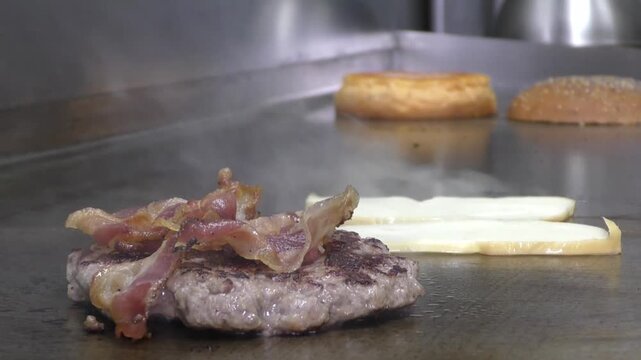 Preparazione di un panino hamburger su piastra. Panino hamburger grigliato con pancetta, cipolla glassata, formaggio e uova