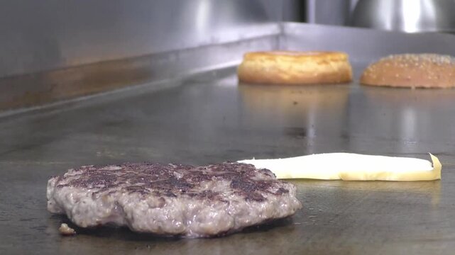 Preparazione di un panino hamburger su piastra. Panino hamburger grigliato con pancetta, cipolla glassata, formaggio e uova