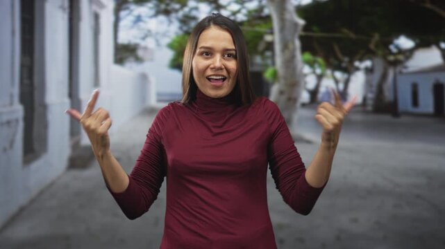 Woman pointing index fingers to her chest and shrugging palms on a street; playful uncertainty self doubt.