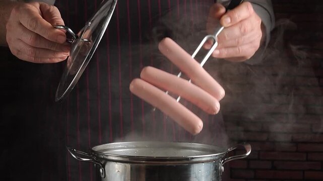 Chef in striped apron lifts sausages from boiling pot with tongs, steam rising in a rustic kitchen setting with brick wall background