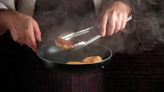 A chef in a striped apron skillfully flips golden brown donuts with tongs in a frying pan, steam rising around them in a well-lit kitchen, demonstrating cooking techniques and kitchen utensils
