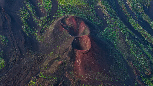 Aerial view of Mount Etna showing volcanic craters with reddish soil and green vegetation on the slopes in Castiglione di Sicilia, Sicily, Italy.