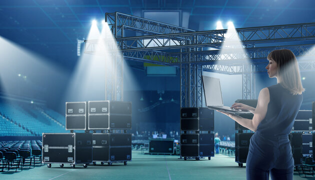 Event production, Stage setup. Coordinator with laptop manages lighting truss and equipment cases inside a concert venue.