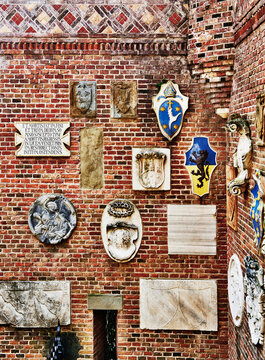 a red brick wall adorned with numerous historical stone artefacts, relief sculptures, and coats of arms in Castello Mackenzie (Mackenzie Castle) built 1893, in Genoa, Italy, Europe 