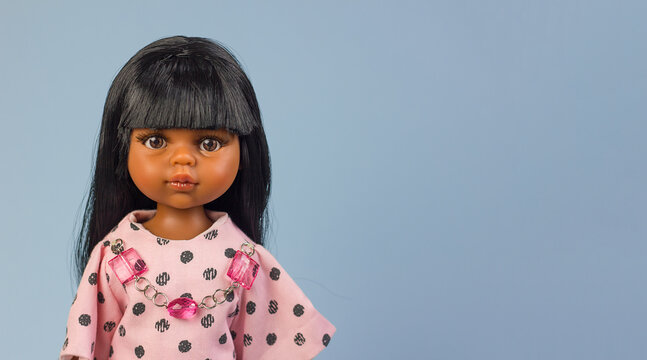 Realistic vinyl toy doll with beautiful dark hair and dark skin in stylish clothes on a blue background, close-up portrait	