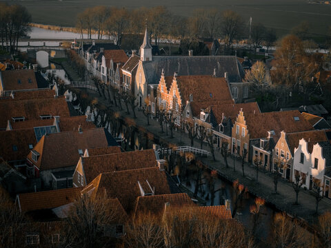 Aerial view of historic red-tiled rooftops and a traditional church along a canal during golden hour in Sloten, Friesland, Netherlands.