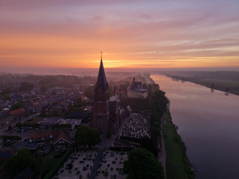 Aerial view of the historic church and Kasteel De Keverberg along the Meuse river during a vibrant sunrise Kessel, Limburg, Netherlands.