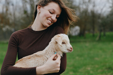 Naklejka premium Goat, kid, woman, outdoor, lifestyle, nature, countryside, portrait, smiling, affection in a sunlit moment as a gentle breeze moves through greenery and calm happiness in a pastoral setting