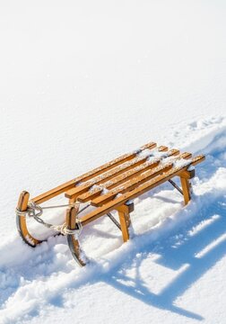 A classic wooden sledge is nestled deeply in fresh white powder snow, ready for winter recreation and fast downhill sliding activities, frost, wooden, hillside